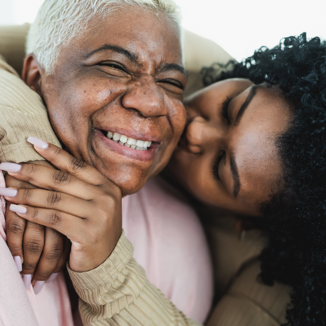 two women hugging, daughter kissing senior mother's cheek